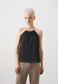 Svart halterneck-top laget av lett stoff med ruftet halslinning, tynne sølvstropper og løs passform. Kombinert med beige bukser.