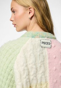 Sweter dzianinowy w pastelowych kolorach: jasna zieleń, róż i biel. Teksturalne wzory obejmują warkocze oraz bąbelki. METKA: "PIECES" z tyłu.