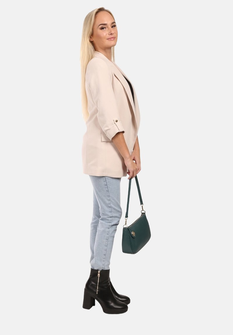 Beige blazer met opgerolde mouwen, zwarte top, lichtblauwe jeans en zwarte platform enkellaarzen, met een kleine groene handtas.