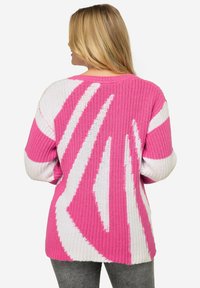 Stickad tröja med en lös passform i rosa och vita zigzag-mönster. Strukturerad tyg med långa ärmar och en bredare halsringning.