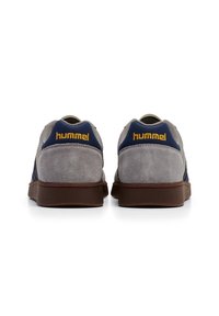 Grijze suède sneakers met marineblauwe accenten en gele branding op de hak. Gearchiveerde zijkanten, ronde neus en een bruine rubberen zool.