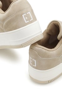 Beige Sneaker mit glatter Textur, weißen Akzenten und einem leeren quadratischen Logo an der Ferse. Dicke Sohle mit einem gemusterten Grip.