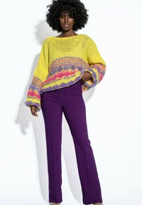 Żółty sweter z wełny, z fioletowymi i różowymi detalami, luźny krój i szerokie rękawy. Połączony z dopasowanymi fioletowymi spodniami. Gładka tekstura.
