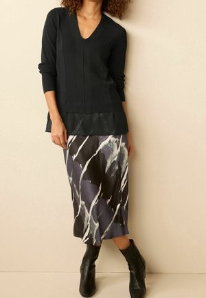 Schwarzer gerippter Pullover mit V-Ausschnitt und Peplum-Saum, kombiniert mit einem gemusterten, seidigen Midirock mit abstrakten Designs in Grau und Weiß.