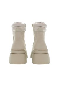 Un paio di stivali beige alla caviglia con tacco spesso, colli imbottiti e cerniere posteriori, mostrati da dietro su uno sfondo bianco.