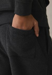 Sorte sweatsuits har et tekstureret stof, ribbede manchetter og en sidelomme med en diskret syning.