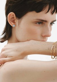 Pendiente de plata con una piedra preciosa azul. Primer plano de una mano descansando sobre el brazo, con pulseras de oro en capas. Textura de piel suave.