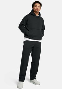 Czarna bluza z kapturem i kieszenią kangurką oraz dopasowane spodnie, o luźnym kroju i gładkiej fakturze, noszone z jasnoszarymi trampkami.