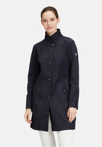 Imperméable mi-long bleu marine avec un col structuré, fermeture à boutons et deux poches latérales. Tissu lisse et léger avec un léger éclat.