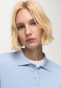 Hellblaues Poloshirt mit Kragen, aus geripptem Stoff. Verfügt über drei Knöpfe am Hals und einen klassischen Schnitt.