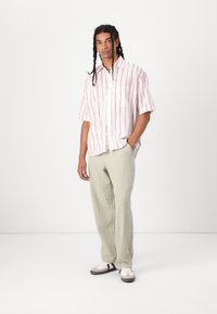 Short-sleeve button-up shirt with red stripes on a white background, paired with light green textured pants and white sneakers with gray accents.