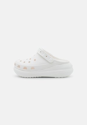 Mocassin blanc à enfiler avec des trous de ventilation, une sangle de talon ajustable et une semelle épaisse et rembourrée, présenté de côté sur un fond uni.