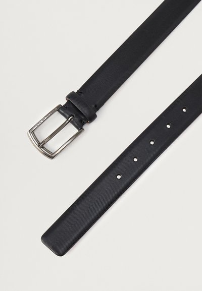 Μαύρη συνθετική ζώνη με υφή ψαροκόκαλο, ασημένια μεταλλική πόρπη και πολλαπλές τρύπες για ρύθμιση μεγέθους. Το άκρο είναι στρογγυλεμένο.