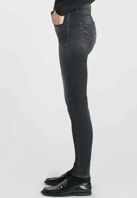 Jean skinny noir taille haute, avec des coutures décoratives sur la poche arrière et une texture en denim lisse. Les chaussures assorties sont brillantes.