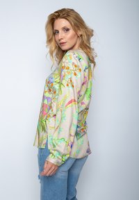 Multicolore bloes met bloemenmotief van lichte stof, met lange mouwen, een relaxed fit en levendige botanische patronen op een beige achtergrond.