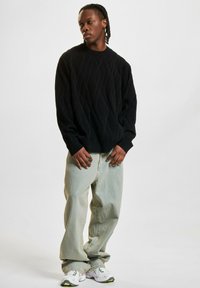 Svart strikket genser med et strukturert diamantmønster, kombinert med lyseblå vide jeans og hvite joggesko.