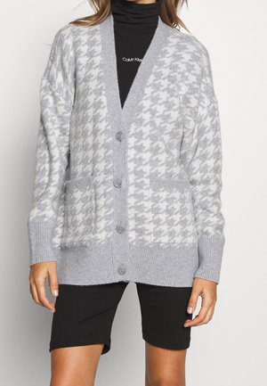 Gray houndstooth cardigan with a v-neck, button closure, and two front pockets. Made of soft knit material with ribbed cuffs.