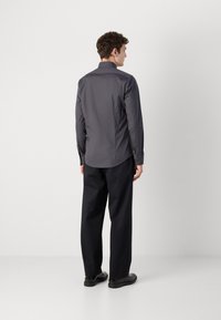 Graues Langarm-Hemd mit strukturiertem Kragen und Rückenpasse, kombiniert mit schwarzen weiten Hosen und schwarzem Schuhwerk.