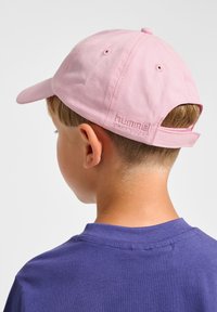 Rosa Baumwollmütze mit gebogenem Schirm und verstellbarem Riemen. Mit geprägtem Markenlogo auf der Rückseite. Hintergrund ist in einer einfarbigen hellen Farbe.