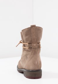 Brune ruskinds ankelstøvle med en afrundet tå, en bundet læderdetalje og en struktureret gummisål. Syning langs hælen.