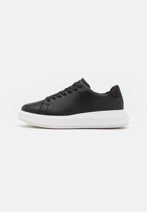 Sneaker en cuir noir avec un bout arrondi, six œillets et une semelle plate-forme blanche. Texture lisse avec des accents minimaux et un design basse.