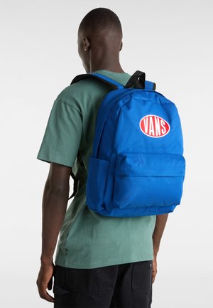 Blå tygryggsäck med en frontficka, förstärkta remmar och en cirkulär Vans-logotyp i rött. Bakvy visar en slät yta och en strukturerad design.