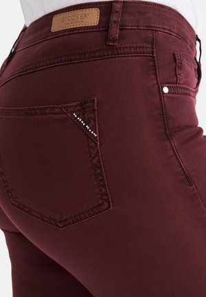 Burgunderfarbene Slim-Fit-Jeans mit einer glatten Textur, ausgestattet mit einer diamantbesetzten Taschenverzierung und einem braunen Lederetikett am Bund.