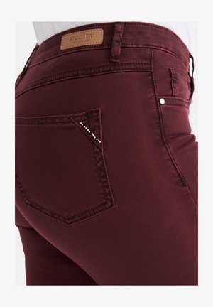 Burgunderfarbene Slim-Fit-Jeans mit einer glatten Textur, ausgestattet mit einer diamantbesetzten Taschenverzierung und einem braunen Lederetikett am Bund.