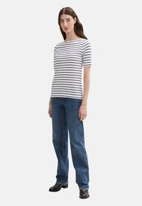 Hvid og navy stribet T-shirt med korte ærmer, sammen med blå jeans og sorte støvler. T-shirten har en rund hals og en afslappet pasform.
