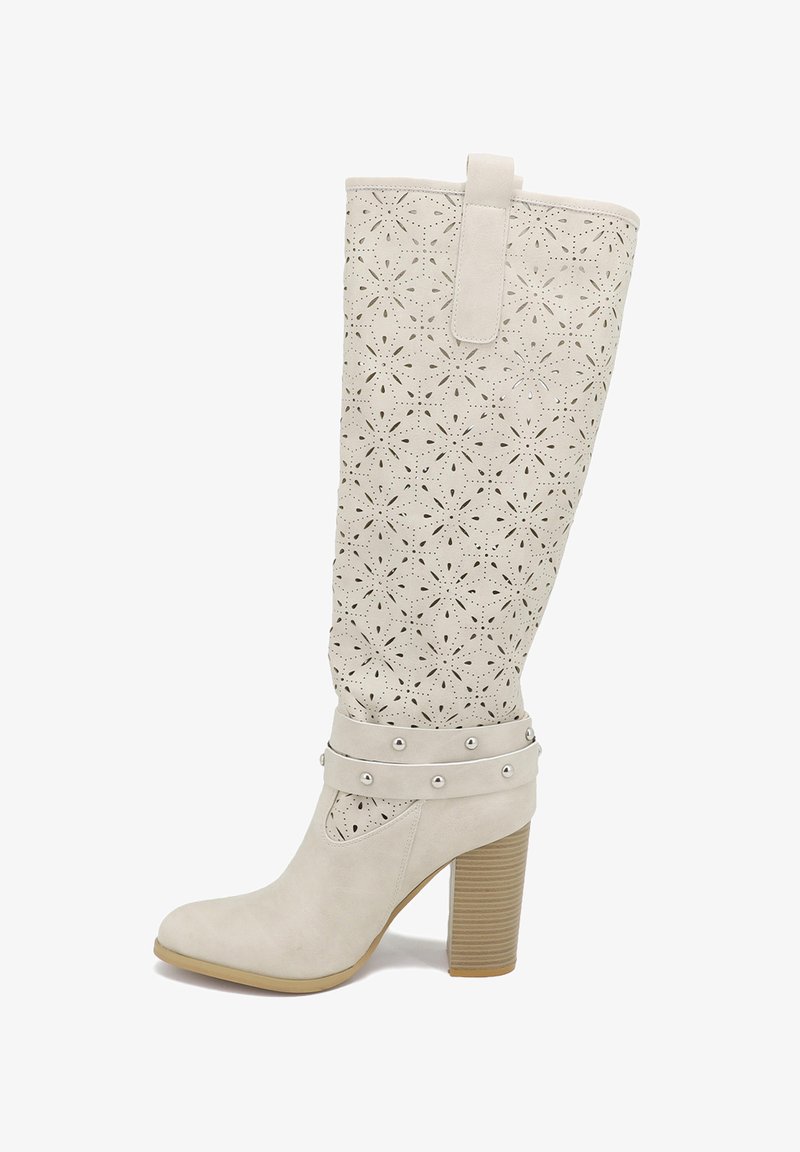 Stivale bianco al ginocchio con motivo floreale a laser, texture liscia, tacco a blocco e cinturini con borchie alla caviglia. Presenta un occhiello per il pull-tab nella parte superiore.
