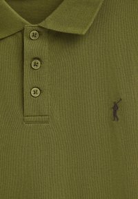 Olivgrön polo-shirt i texturerat tyg, med en treknapplisted och en liten broderad logotyp av en figur i brunt.