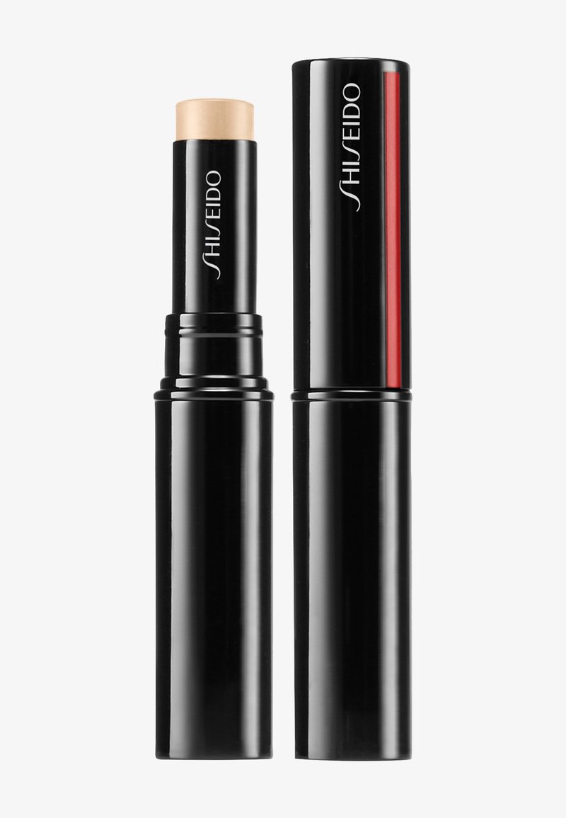 Shiseido foundation stick dalam kemasan hitam berbentuk silinder. Produk ini menampilkan stik dengan warna kulit dan desain ramping dengan aksen merah.
