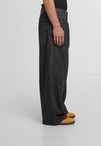 Black oversized denim jeans with a high waist, straight leg, and prominent stitching details. Worn with yellow shoes.