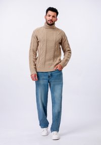 Pull en laine beige à col roulé en tricot, design texturé, associé à un jean droit bleu clair et des chaussures de sport blanches.
