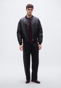 Juoda bombonešio striukė su siuvinėta detalė, derinama su tamsiai raudonu apvalia kaklo megztiniu ir laisvomis juodomis kelnėmis. Avalynė – tamsiai rudi odos stiliaus batai.