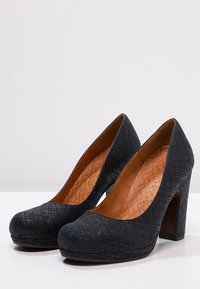 Zapatos de tacón alto negros con parte superior texturizada, punta redonda y tacón de madera sólido. El interior cuenta con un forro marrón claro con un patrón.