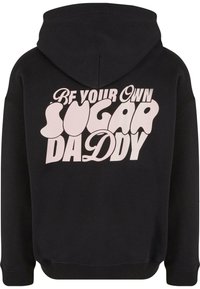 Hanorac negru cu un design grafic roz pe spate, care spune "Fii propriul tău sugar daddy". Material gros și moale, cu o croială lejeră.