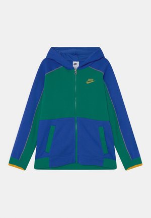 Sudadera con cremallera de Nike en azul y verde, con un acento amarillo en los puños, dos bolsillos frontales y una capucha. Tejido suave con costuras en contraste.