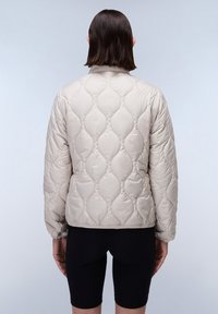 Beige gewatteerde jacket met een rond patroon, elastische manchetten en zoom. Glad, glanzend materiaal, met een hoge kraag en zonder zichtbare sluitingen.