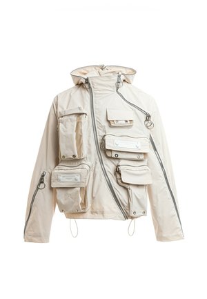 Chaqueta beige con capucha con múltiples bolsillos utilitarios con cremallera y botones a presión, cremallera delantera asimétrica y detalles de tiradores en forma de anilla plateada.