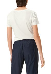 Weißes kurzärmeliges T-Shirt mit rundem Halsausschnitt, kombiniert mit navyblauen elastischen Bundhosen. Glatte Textur, einfaches Design, keine sichtbaren Muster.