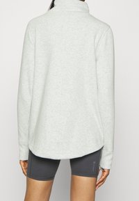 Pulóver de forro polar gris claro con cuello alto, corte relajado, aberturas laterales y mangas largas, combinado con pantalones cortos deportivos gris oscuro.