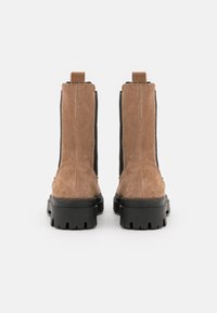 Bruna mockaskor med ankellängd, elastiska sidopaneler och svarta gummisulor. Har en strukturerad yta och en robust design för stöd.