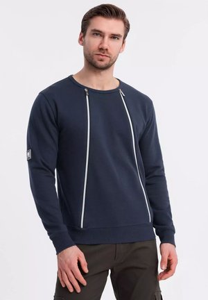 Mörkblå sweatshirt med långa ärmar, med två vita dragkedjor framtill och ribbade ärmslut. Minimalistisk design med logodetalj.