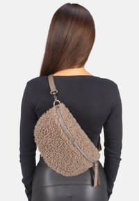 Braune, strukturierte Umhängetasche aus weichem, flauschigem Material mit einem diagonalen Reißverschluss und einem grauen Riemen. Akzentuierter Reißverschluss-Detail.