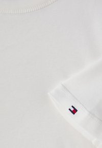 Hvit bomull T-skjorte med ribbet rund hals og korte ermer. Merkbar detalj: lite brodert logo i rødt, hvitt og blått på ermet.