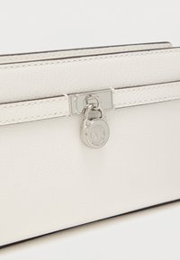 Bela teksturirana usnjena pravokotna torbica s srebrno opremo, ki ima zapiranje s sponko in okrogel logotip kot poudarek.