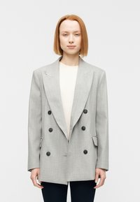 Blazer gris croisé en tissu texturé, dot é de grands boutons noirs, de larges revers et de deux poches avant.