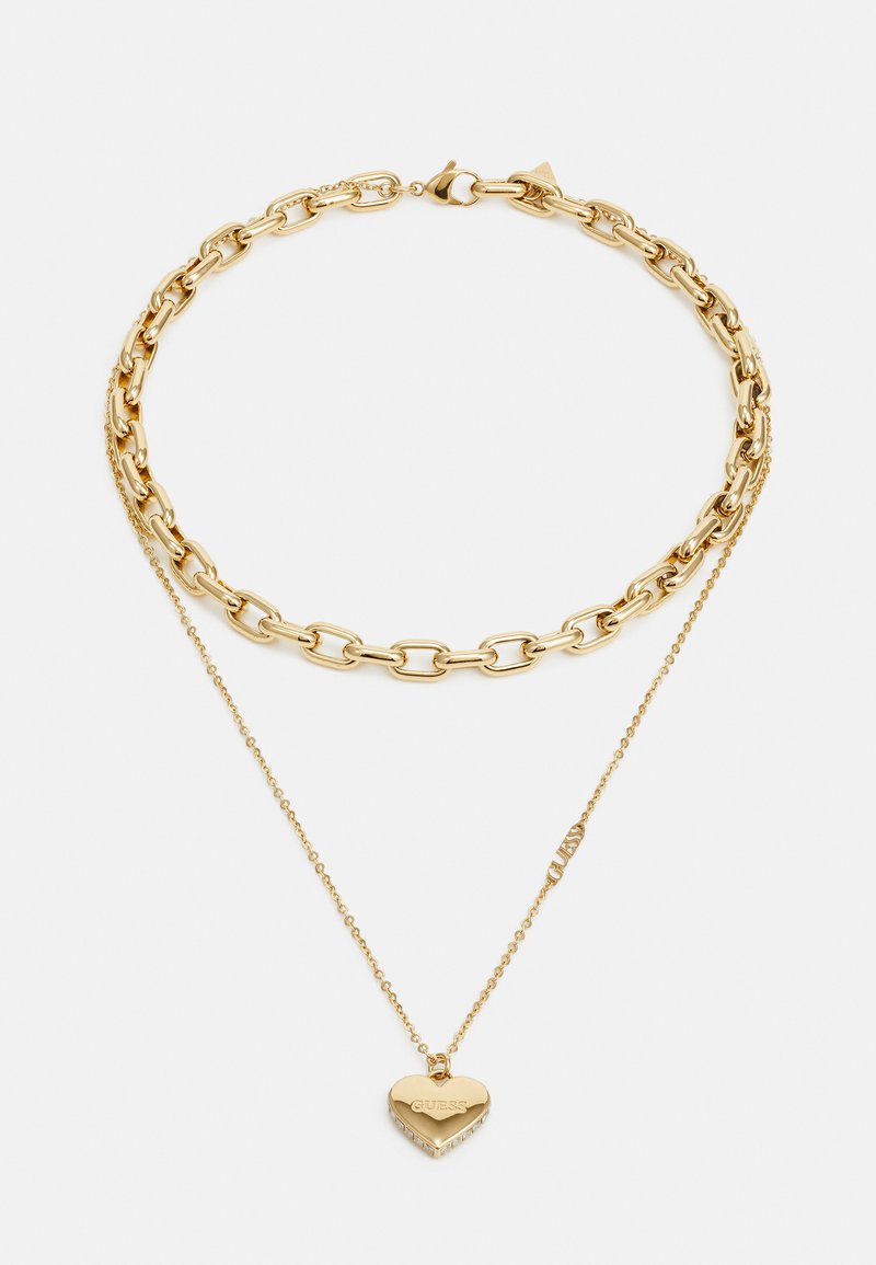 Collana in tonalità oro con una catena spessa con anelli lisci, abbinata a una catena delicata che sostiene un ciondolo a forma di cuore con accenti di pietra.