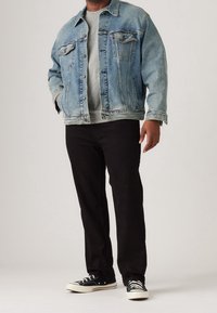 Chaqueta de mezclilla azul claro, sudadera gris, pantalones negros y zapatillas negras. La chaqueta tiene dos bolsillos delanteros y cierre de botones.